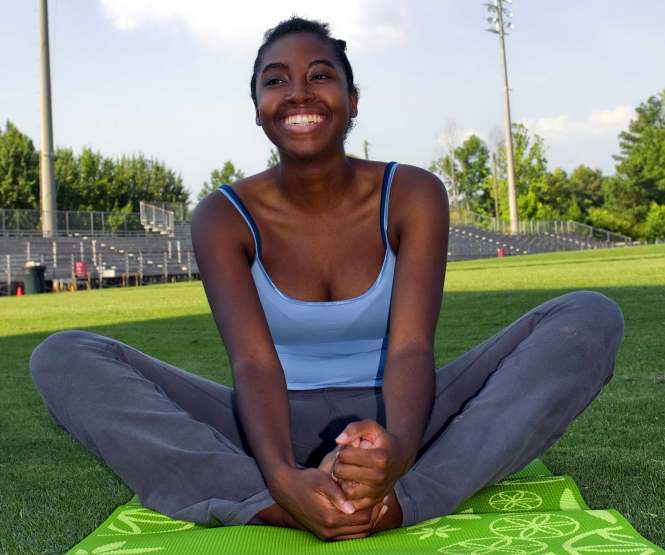 Woman pictured here seated on a bright green mat on the grass in